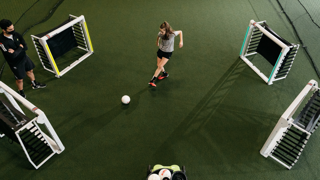 woman practicing kicking balls between 4 goalposts